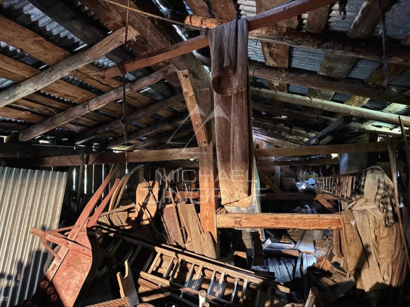 Intérieur d'une vieille ferme à rénover, avec des poutres en bois et des objets anciens entassés.