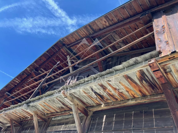 Detail of the wooden structure of an old farmhouse to be renovated in Megève, with a blue sky in the background.