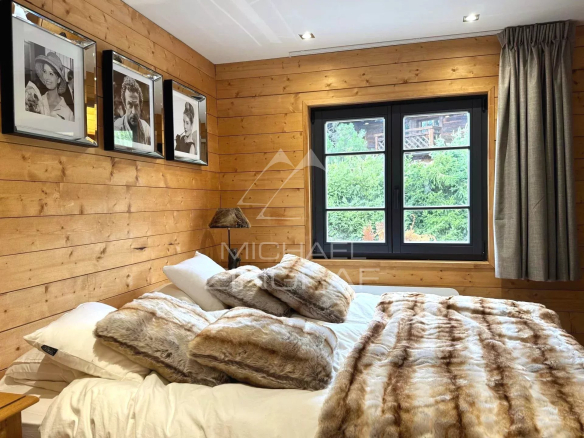 Bedroom in a renovated chalet in Megève with wooden walls and photo frames.