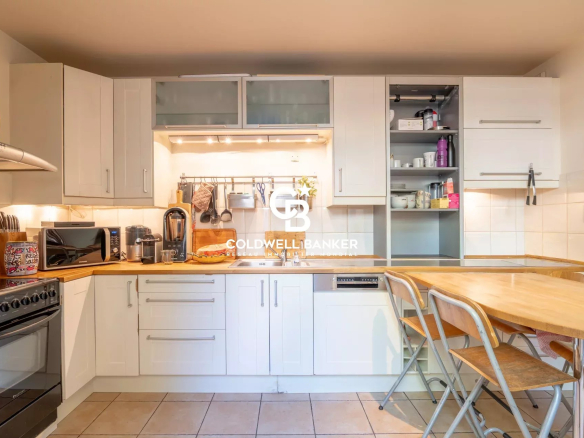 Bright white kitchen with wooden countertops, appliances, and open-shelving pantry; a wooden dining table with metal chairs on the right.