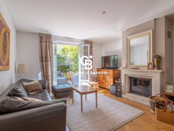 Living room with a gray leather sofa and matching ottoman facing a fireplace and TV, bright French doors open to a garden patio outside.