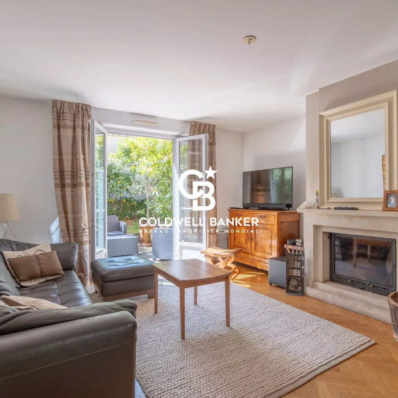 Living room with a gray leather sofa and matching ottoman facing a fireplace and TV, bright French doors open to a garden patio outside.