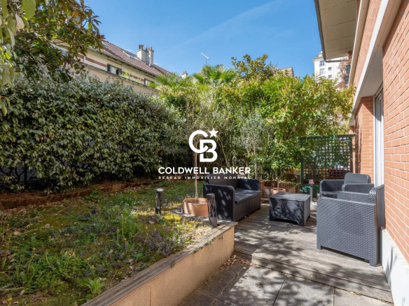 Urban garden patio with wicker seating and potted trees along a brick house, logo of Coldwell Banker centered in the scene.
