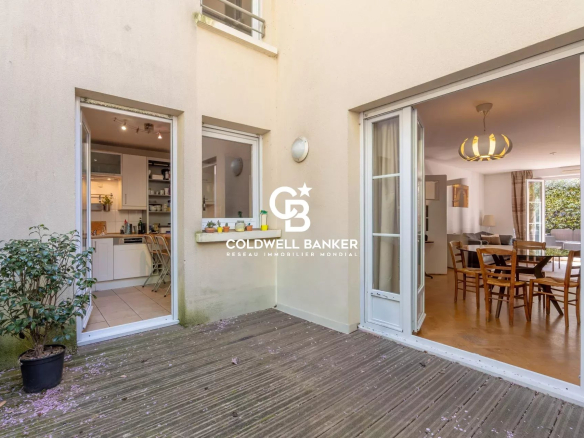 Patio with a wooden deck and two open doors: left shows a white kitchen, right opens to a dining room; Coldwell Banker branding on the wall between.
