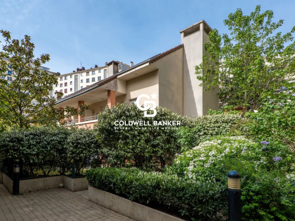Residential building with a manicured garden, hedges, and a paved walkway under a blue sky; Coldwell Banker logo overlayed in the center.