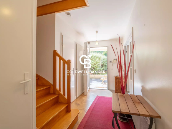 Entry hallway with a wooden staircase on the left, a red runner rug, and a glass door opening to a sunny garden.