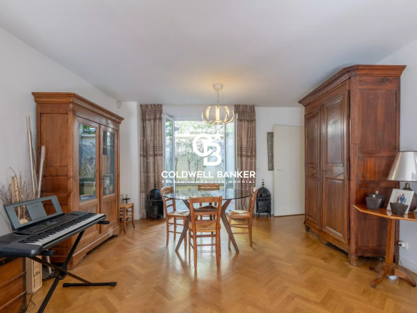Living room with parquet floor, two large wooden wardrobes, a glass-front cabinet, a round dining table with four chairs, and a keyboard on a stand by the left wall.