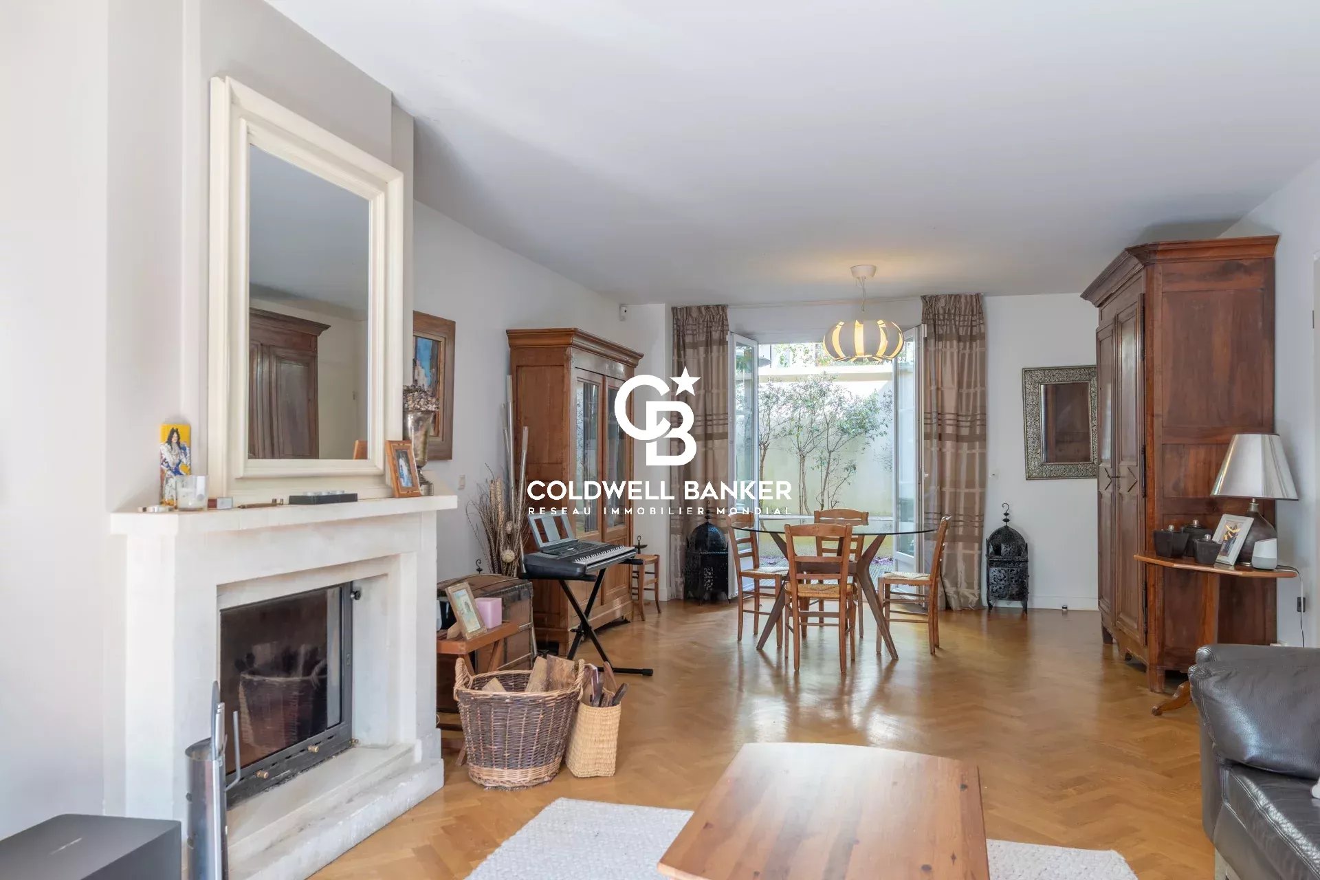 Bright living room with a white fireplace, wooden cabinets, and a round dining table by glass doors to a garden.09