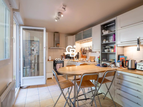 Bright kitchen with a wooden island table and metal stools, white cabinets, and a glass door leading to outside.