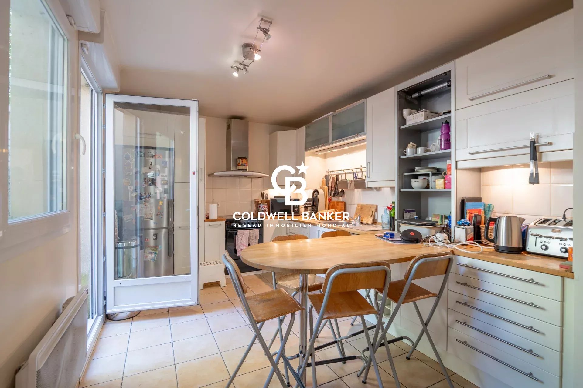 Bright kitchen with a wooden island table and metal stools, white cabinets, and a glass door leading to outside.