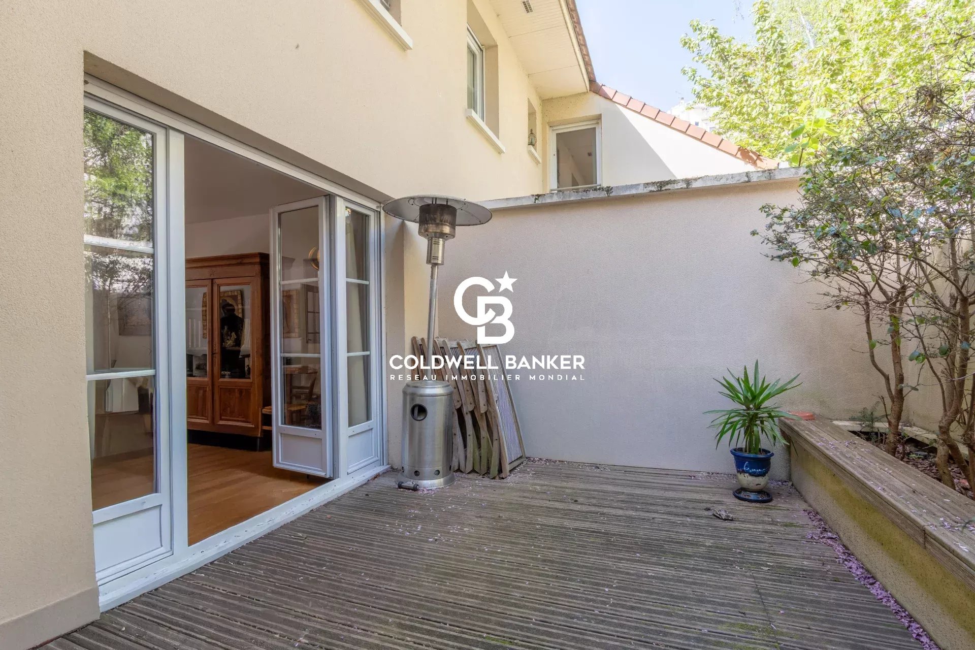 Patio area of a house with open sliding glass doors, a tall outdoor heater, and a stacked wood display on a wooden deck.