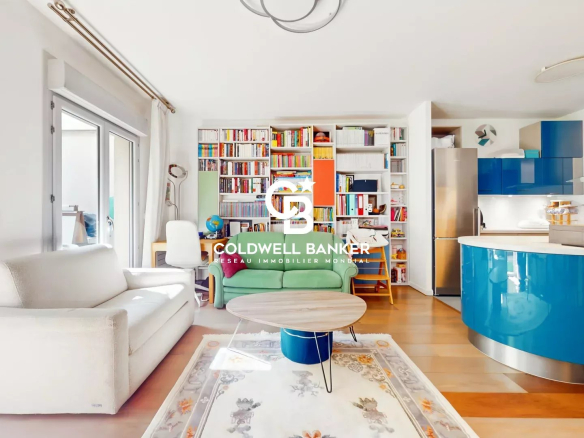 Open-plan living area with a white sofa, green chair, and a tall bookcase wall, leading to a blue curved kitchen island and fridge; watermark in center.