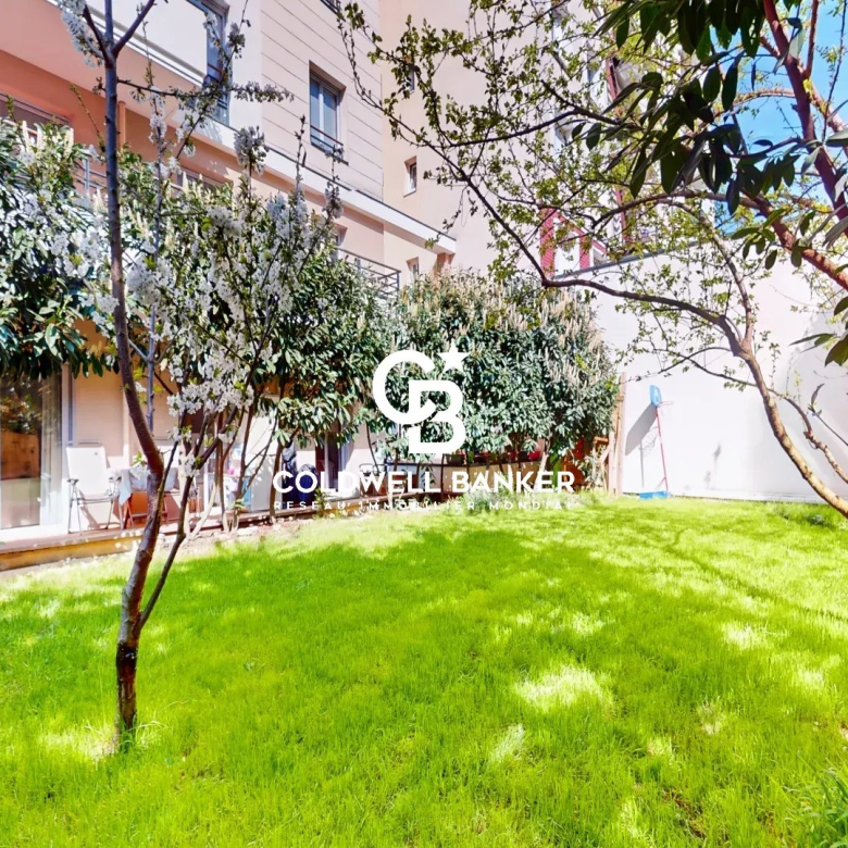 Sunny residential courtyard with a well-kept green lawn, trees, and a glass-walled patio area along the building; Coldwell Banker logo overlay.