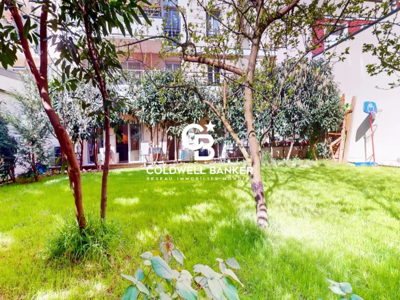 Green grassy courtyard with several trees and shrubs, bordered by white walls and apartment balconies, a small basketball hoop on the right.