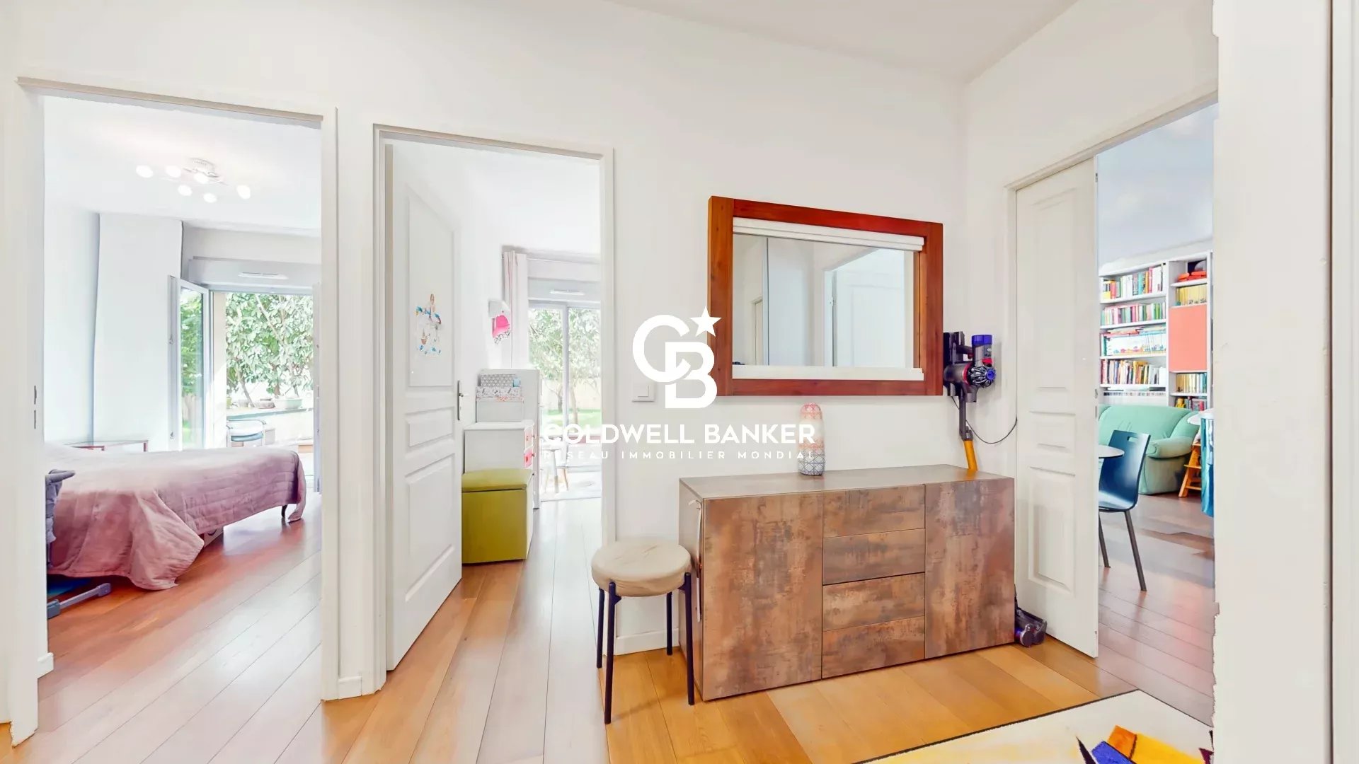 Bright white hallway with a rustic wooden sideboard and a large mirror, doors open to a bedroom and a living space.