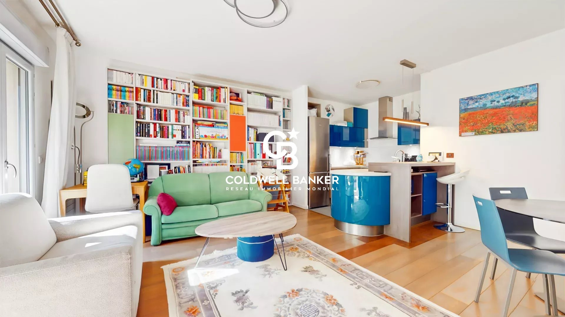 Open-concept living area with a wall of bookshelves, a green sofa, and a round coffee table; blue kitchen island in the background.