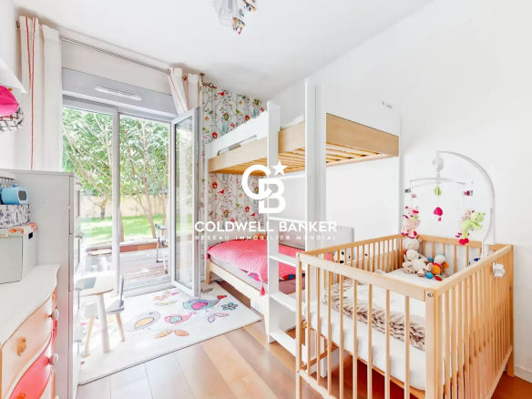Bright children's bedroom with white walls, a wooden bunk bed and a wooden crib, and a white dresser with colorful drawers near sliding glass doors to a green garden exterior