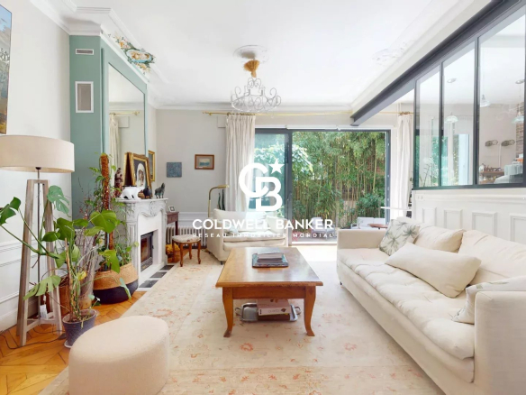 Intérieur d'une maison familiale avec salon lumineux et jardin visible à travers de grandes fenêtres.