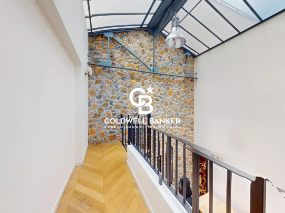 Intérieur d'une maison loft avec murs en pierre et verrière, vue de l'escalier.