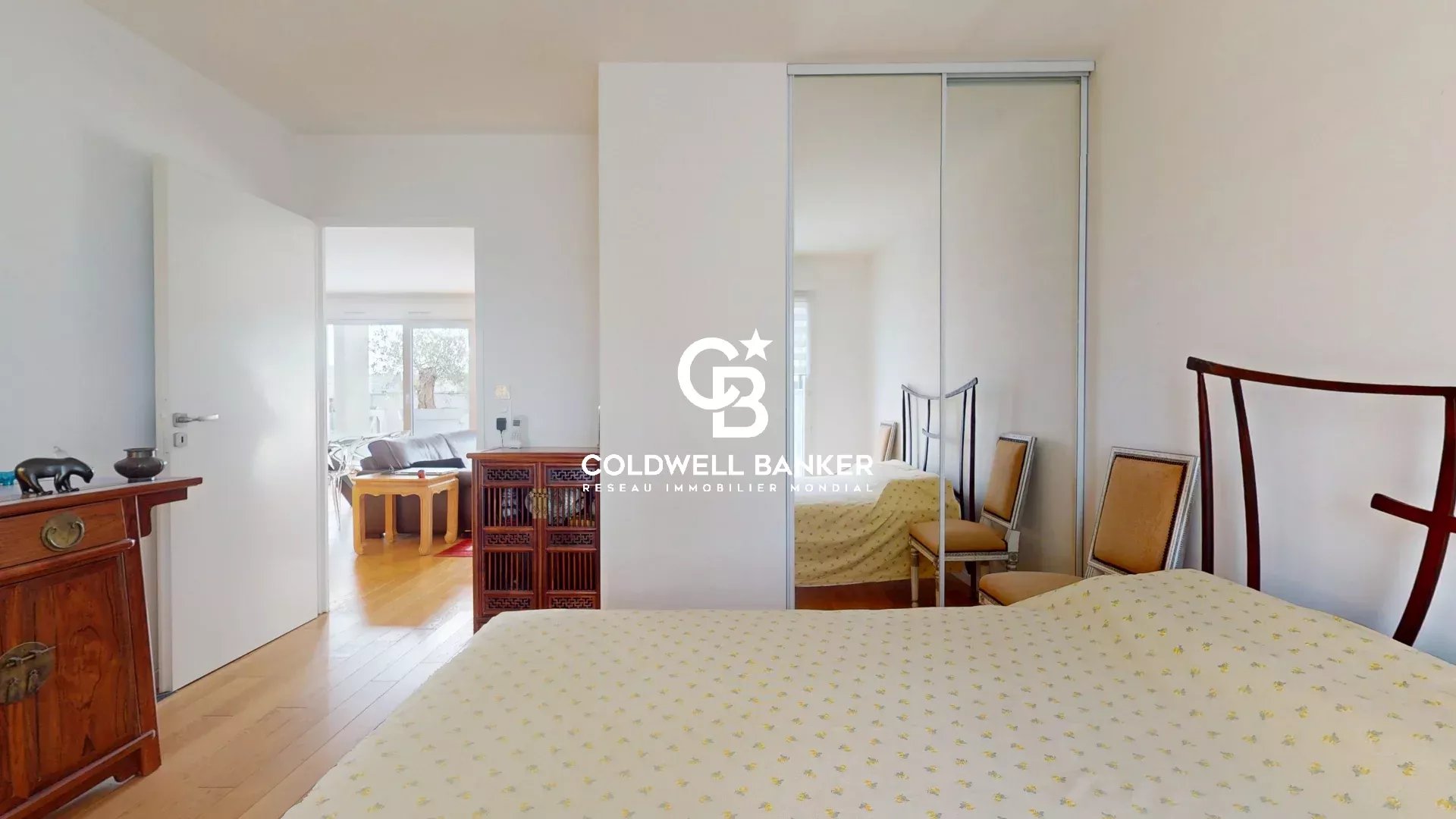 Chambre d'un appartement lumineux avec mobilier en bois et miroir, montrant un espace de vie.