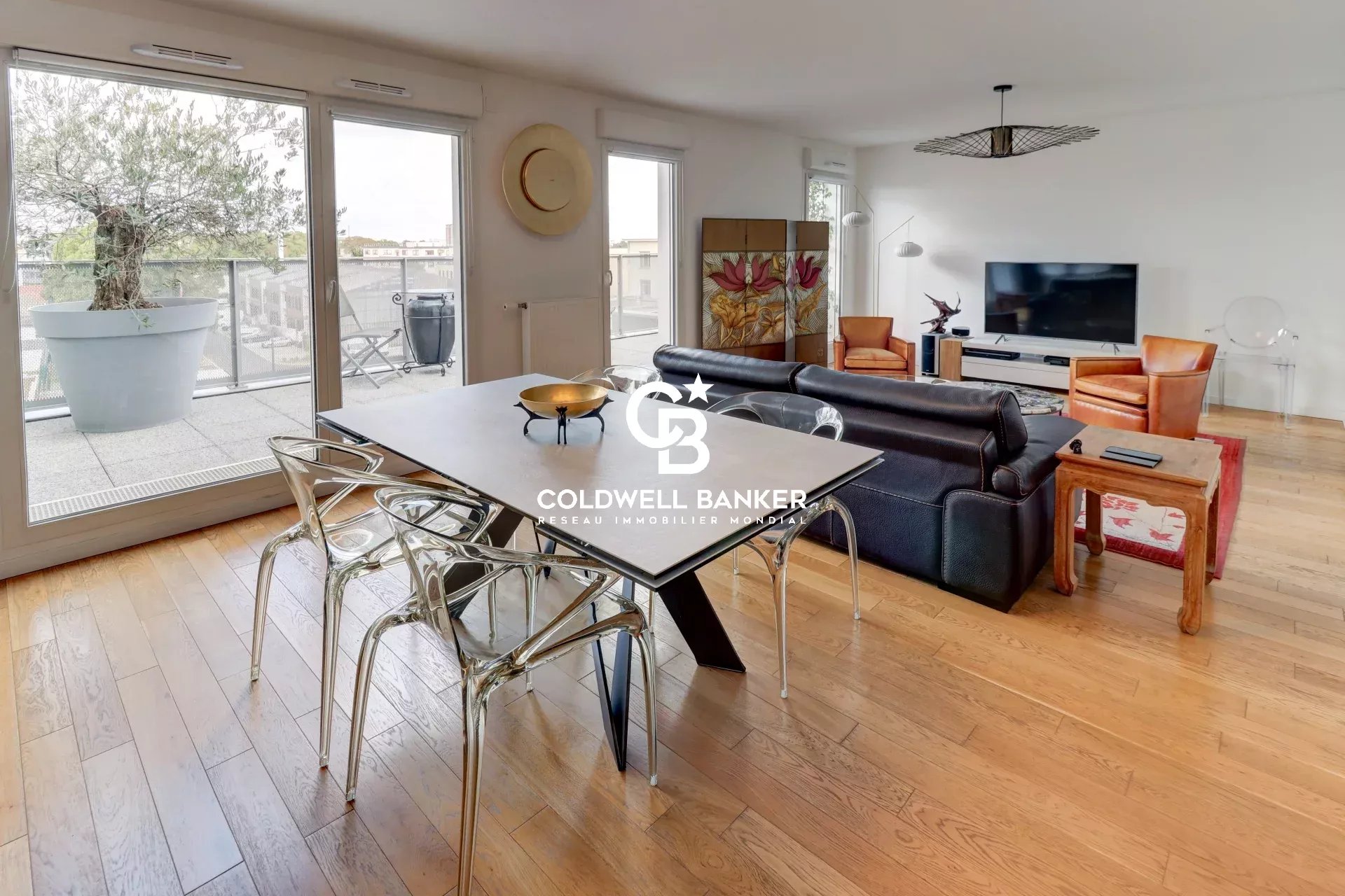 Intérieur d'un appartement lumineux avec salon et salle à manger, fenêtres donnant sur une terrasse.