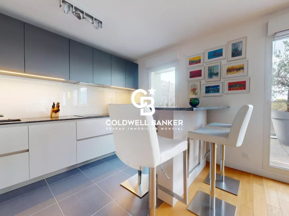 Cuisine moderne d'un appartement avec bar et chaises hautes, fenêtres donnant sur une terrasse.