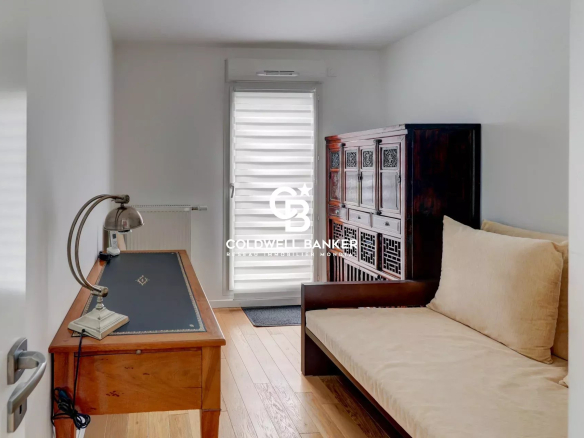 Intérieur d'un appartement lumineux avec un bureau et un canapé, accès à une terrasse.