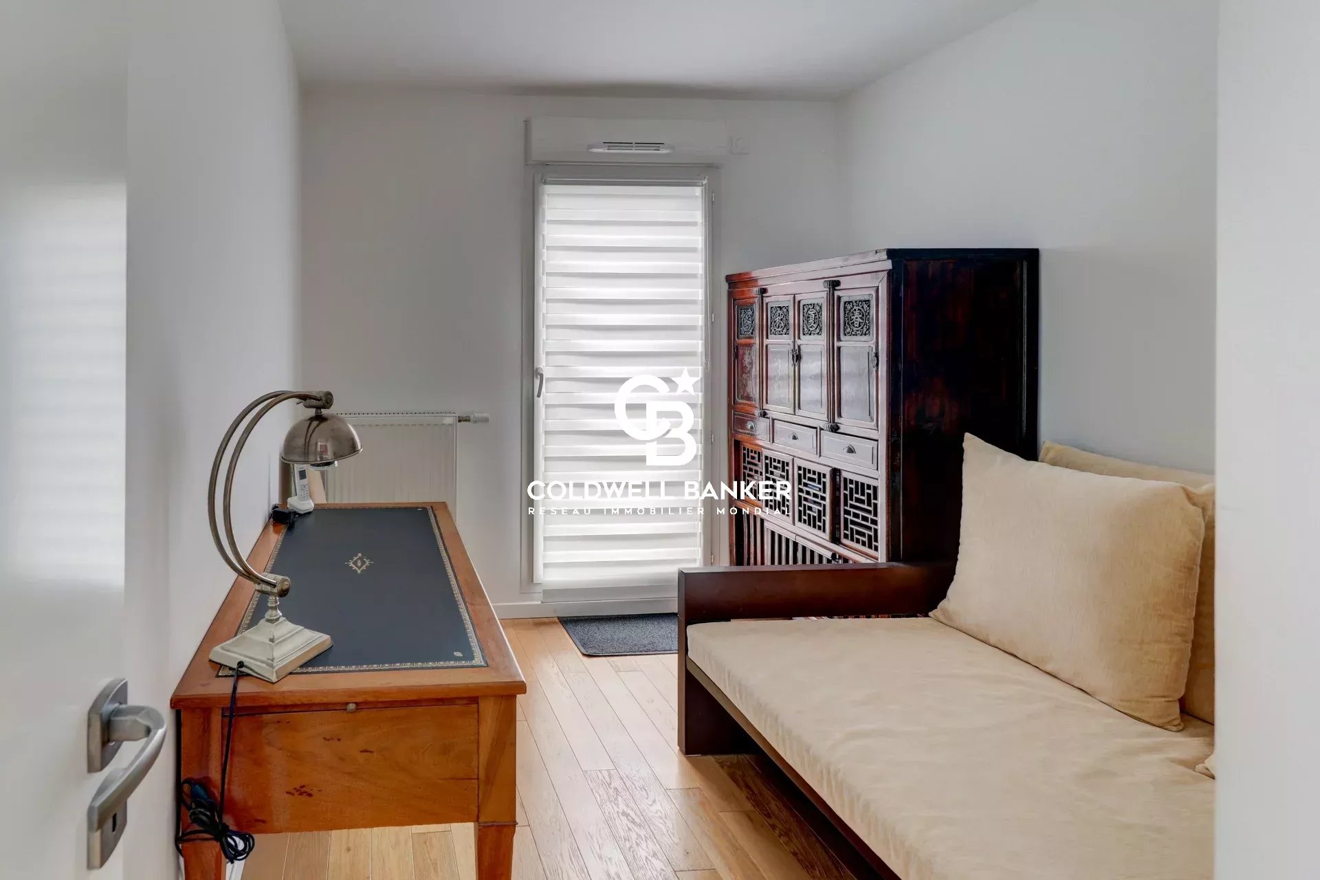 Intérieur d'un appartement lumineux avec un bureau et un canapé, accès à une terrasse.