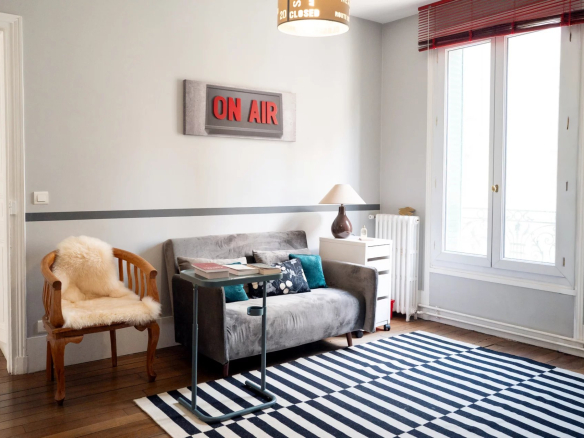 Intérieur d'une maison à Suresnes avec un salon lumineux, un canapé gris et un tapis rayé.