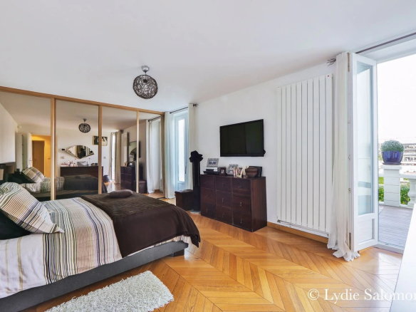 Chambre d'une maison rénovée avec parquet, télévision et accès à un balcon.