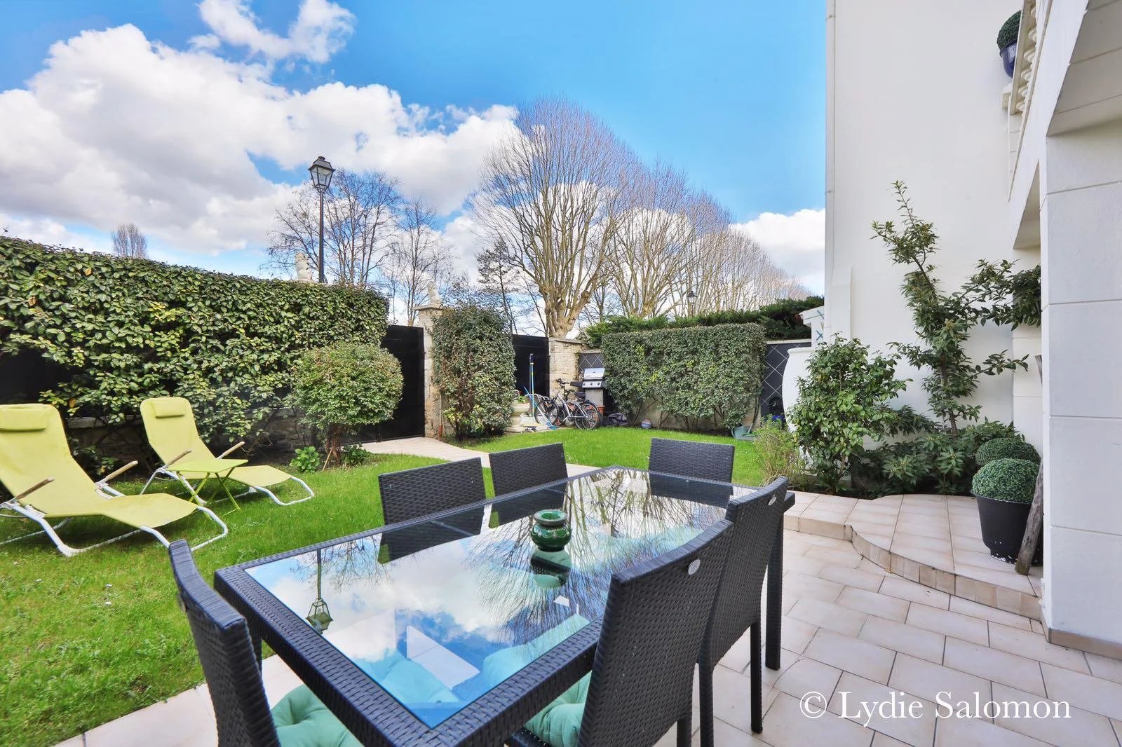 Terrasse de maison à Joinville-le-Pont Terrasse avec table et chaises, jardin verdoyant et ciel bleu, maison à Joinville-le-Pont.