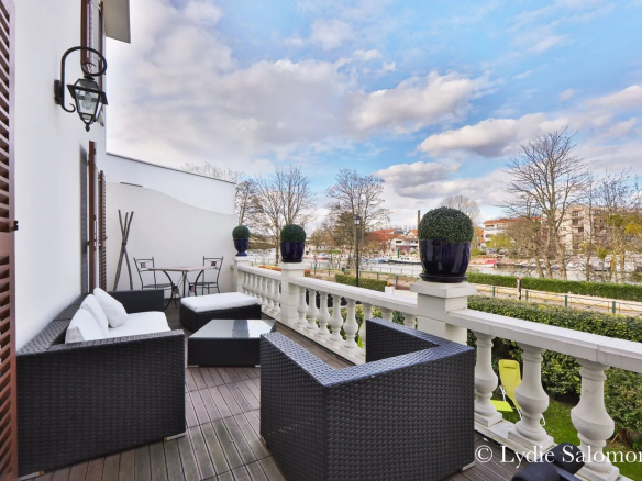 Terrasse d'une maison rénovée avec mobilier en osier, vue sur la Marne à Joinville-le-Pont.
