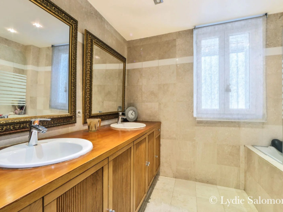 Salle de bain spacieuse avec double vasque et baignoire, murs en pierre beige.