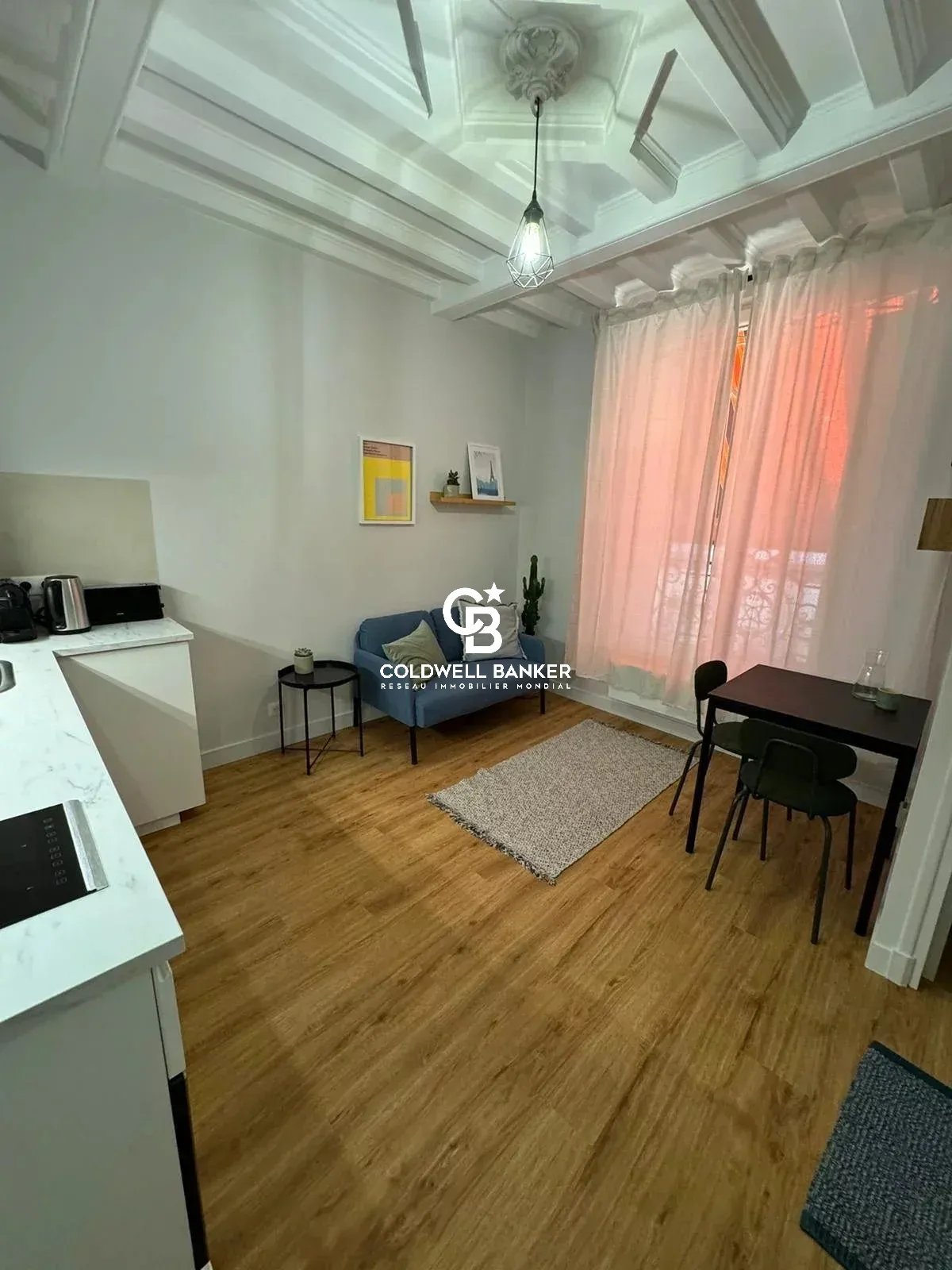 Studio rénové à Montrouge Intérieur d'un studio rénové avec coin cuisine, table et chaises, et lumière naturelle.