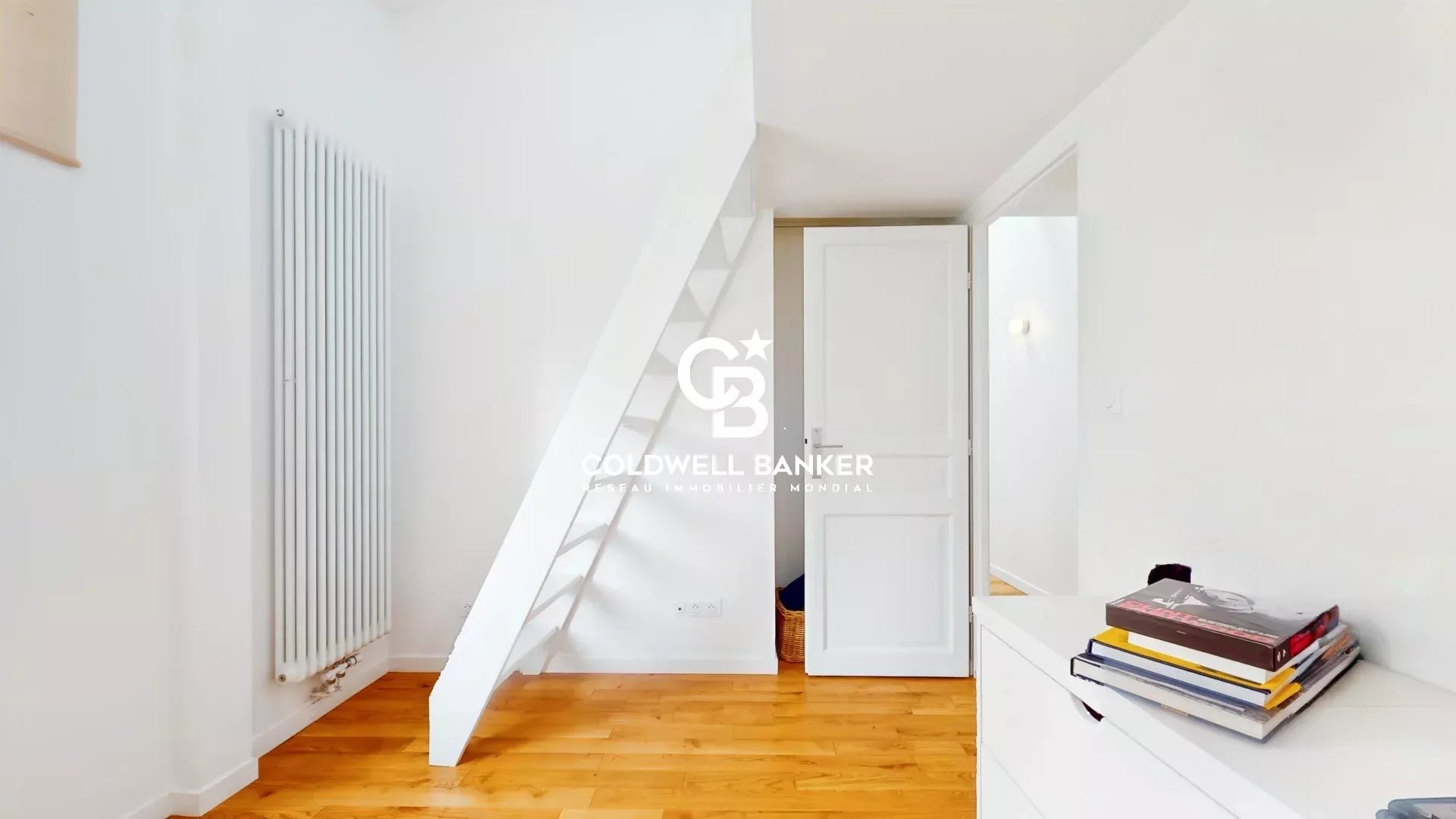 Intérieur d'une maison avec un escalier et des murs clairs, parquet en bois.