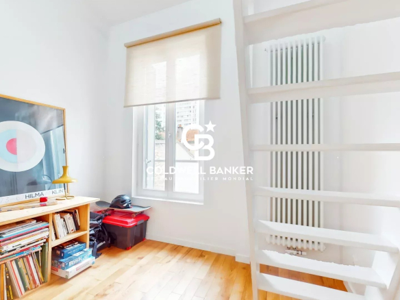 Intérieur d'une maison à Malakoff avec un escalier blanc et une étagère remplie de livres.