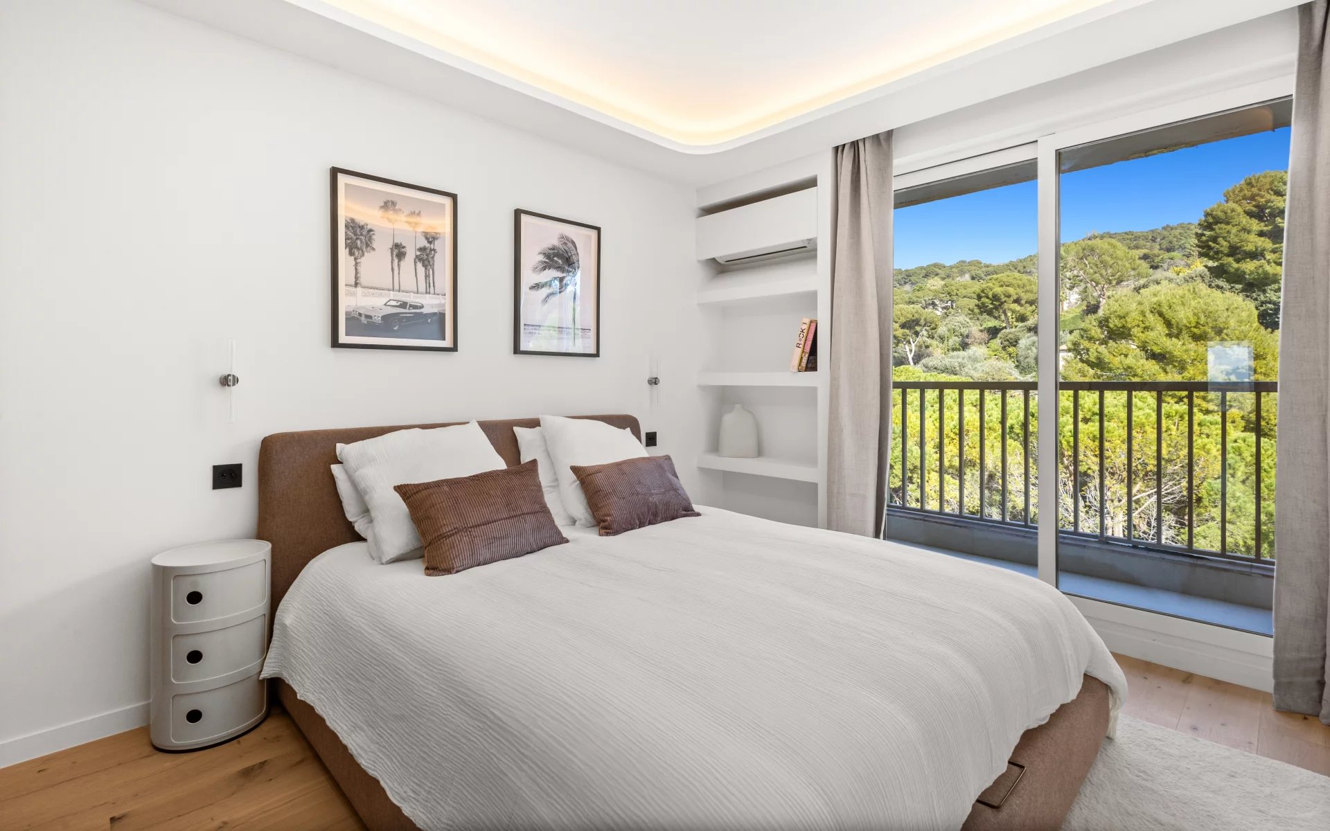 Bright bedroom with a large glass sliding door to a balcony and a view of green trees outside.