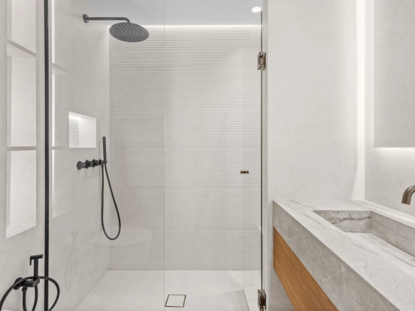 Modern bathroom with a glass-walled shower, a large black rainfall showerhead, and a marble countertop vanity.