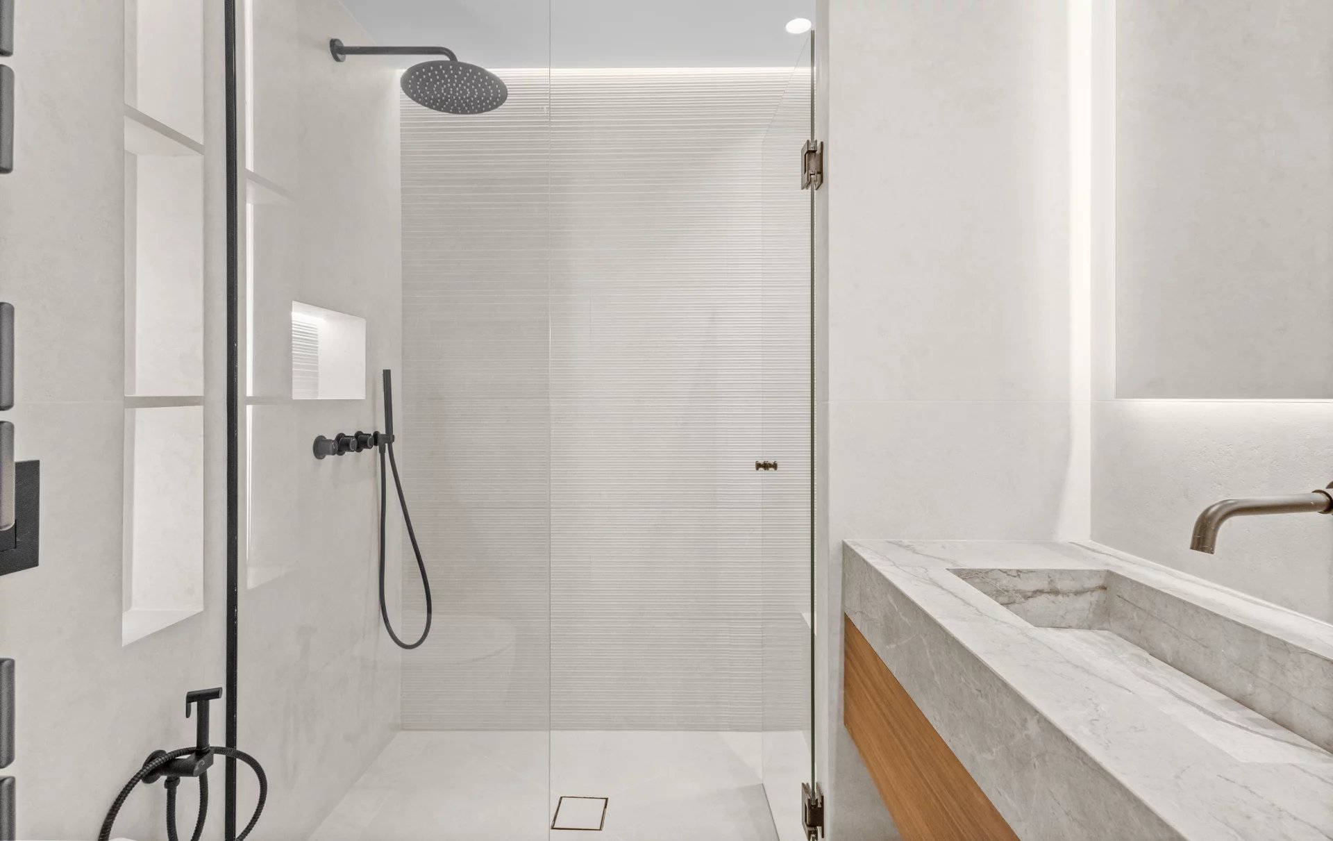 Modern bathroom with a glass-walled shower, a large black rainfall showerhead, and a marble countertop vanity.