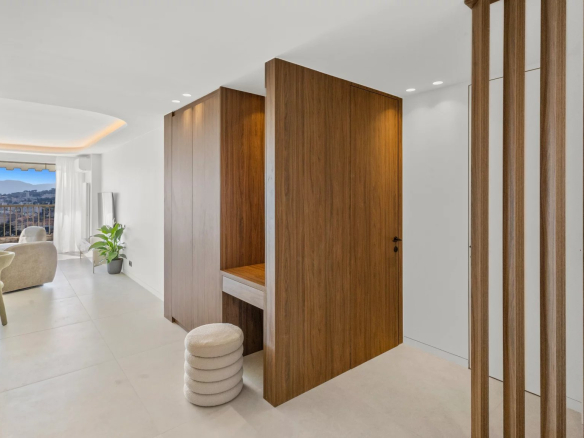 Bright minimalist hallway with tall wooden room dividers, a small desk area, and a seating nook by a balcony window.