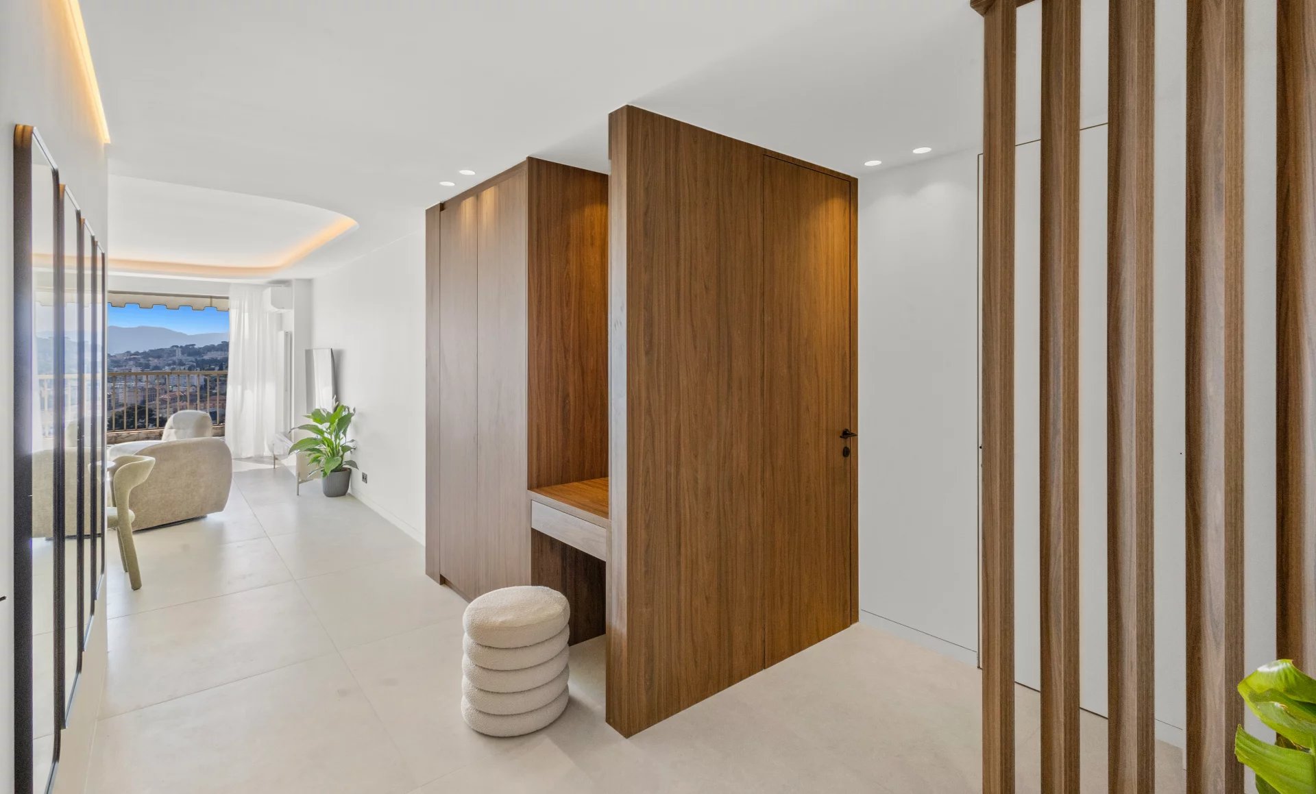 Bright minimalist hallway with tall wooden room dividers, a small desk area, and a seating nook by a balcony window.