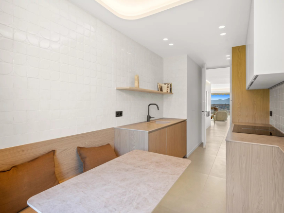 Bright modern kitchen with white tiled walls, light wood cabinets, a marble table, and a bench with brown cushions.
