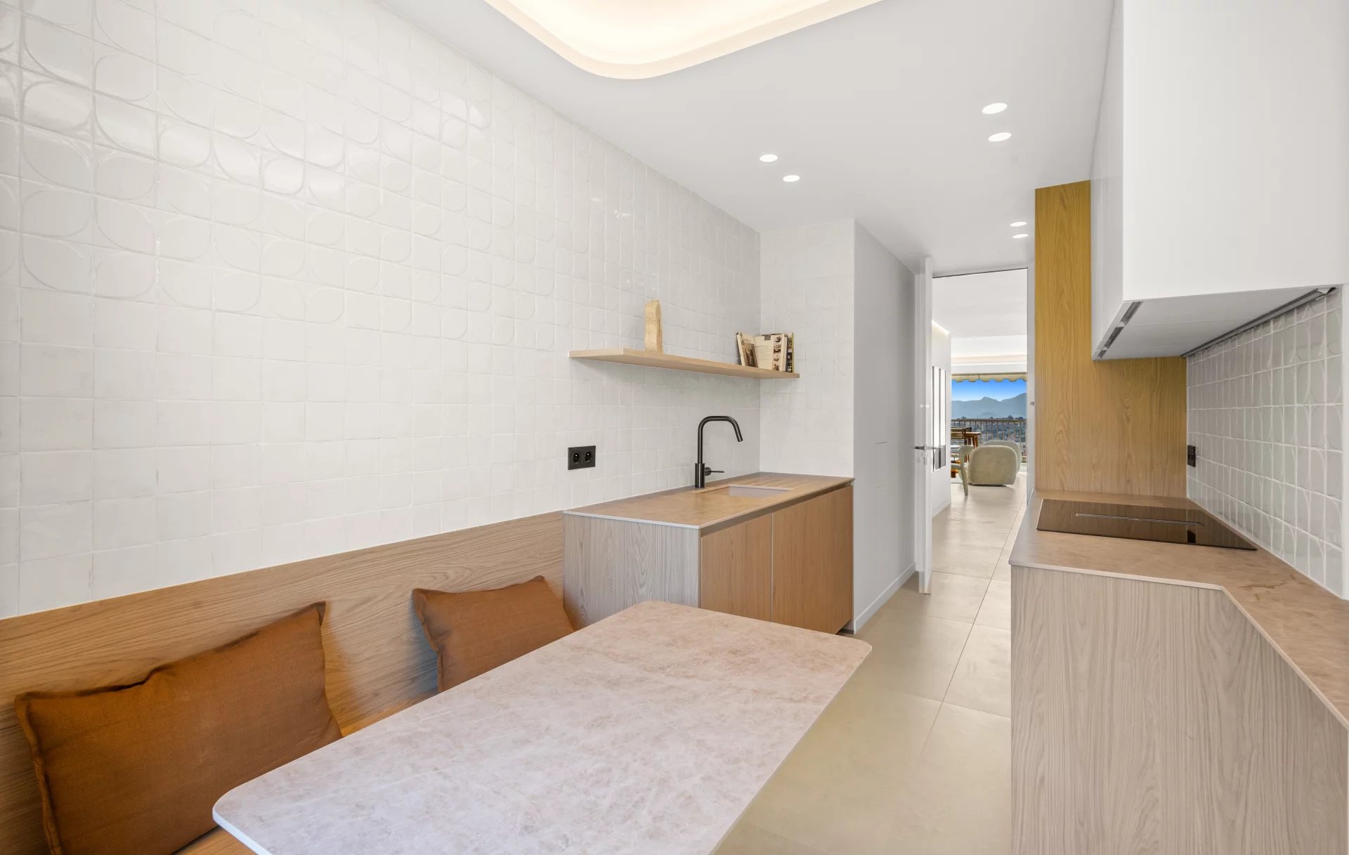Bright modern kitchen with white tiled walls, light wood cabinets, a marble table, and a bench with brown cushions.