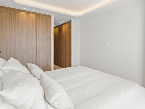 Modern bedroom with white bedding, a large wood-paneled wardrobe, and a doorway to a hallway.