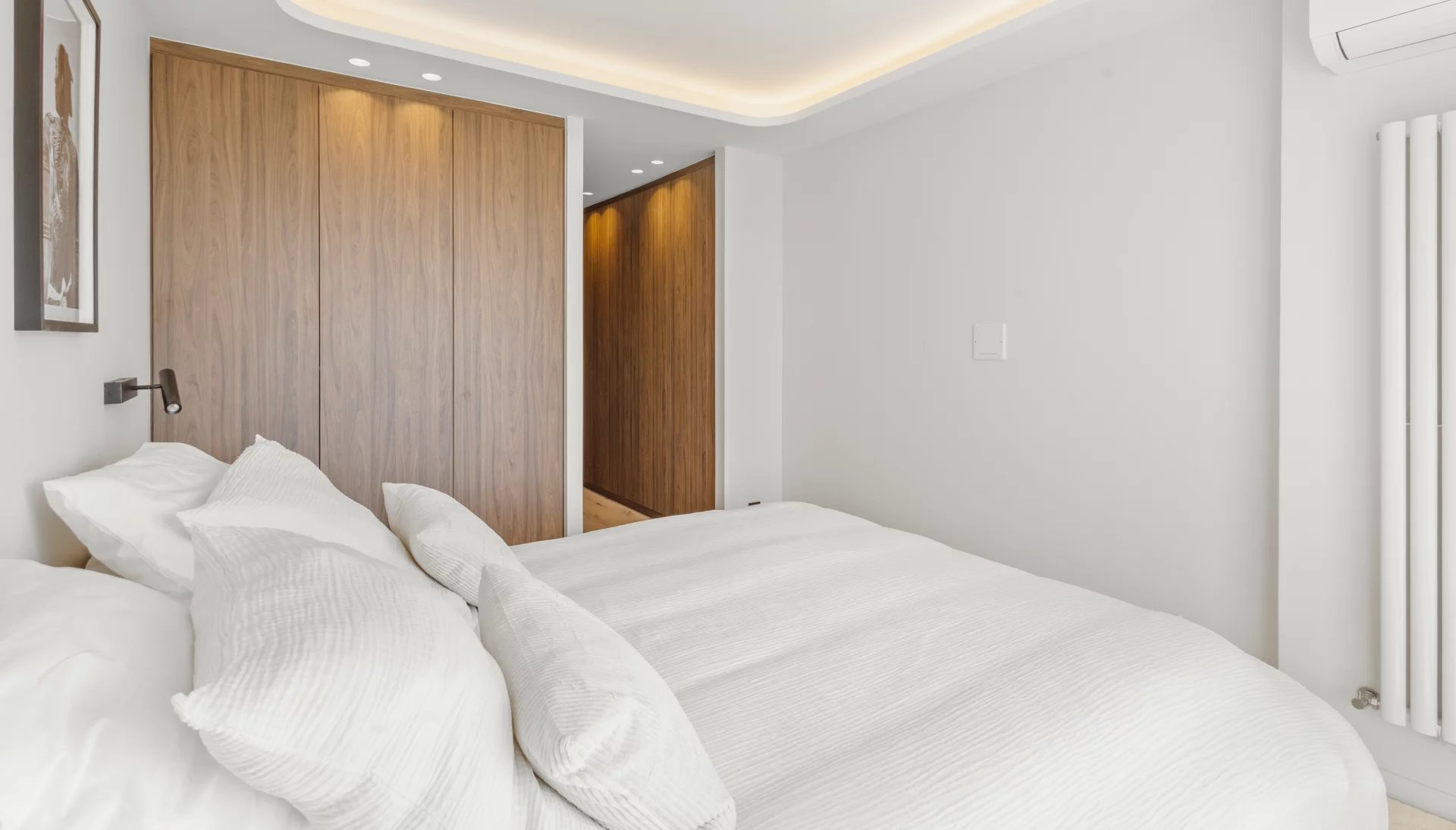 Modern bedroom with white bedding, a large wood-paneled wardrobe, and a doorway to a hallway.