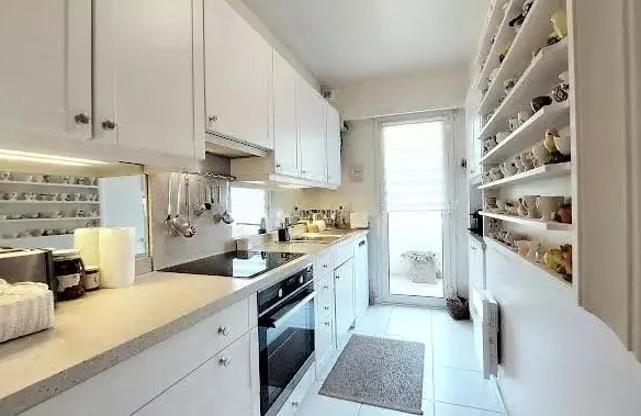Bright white galley kitchen with upper and lower cabinets, left-side appliances, and a tall pantry wall of labeled jars on the right.