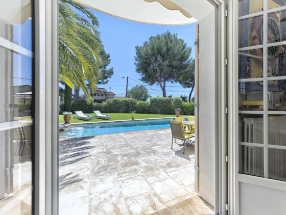 View of a swimming pool and garden from inside a bastide in Le Cannet, with palm trees and sun loungers.