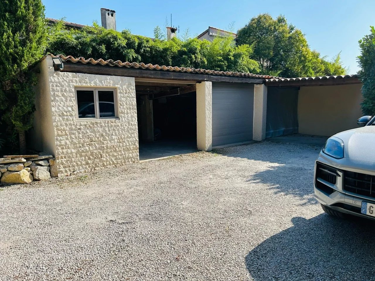 Garage at a villa in Mougins with a gravel driveway and greenery around.