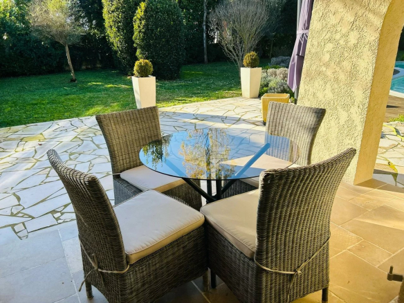 Terrasse d'une villa à Mougins avec table en verre et chaises en osier, vue sur le jardin.