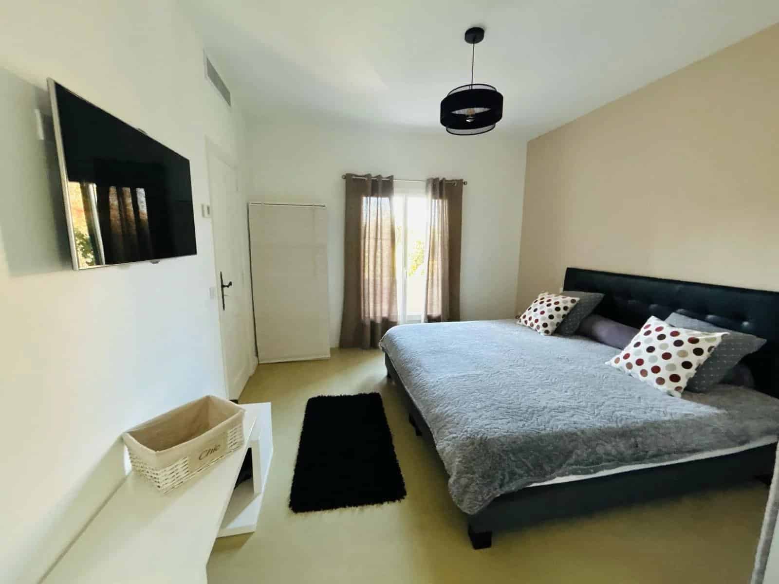 Chambre d'une villa à Mougins avec lit double, télévision et fenêtres donnant sur l'extérieur.
